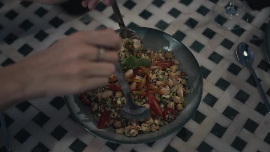 Hands mix chickpea salad with colorful vegetables in a bowl
