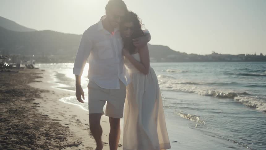 A couple strolls handinhand along a sunlit beach casting soft shadows on the wet sand