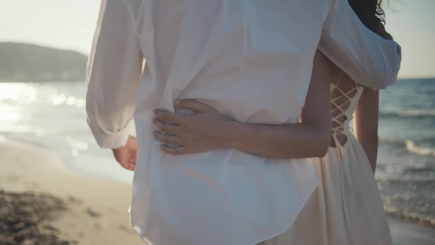 Couple hugs while walking on the beach near the surf during the daytime