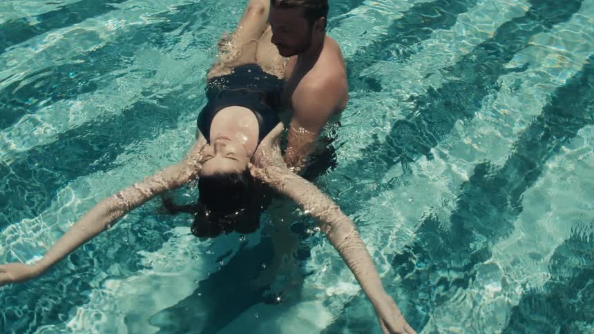 A couple floats in a pool the man supporting the woman