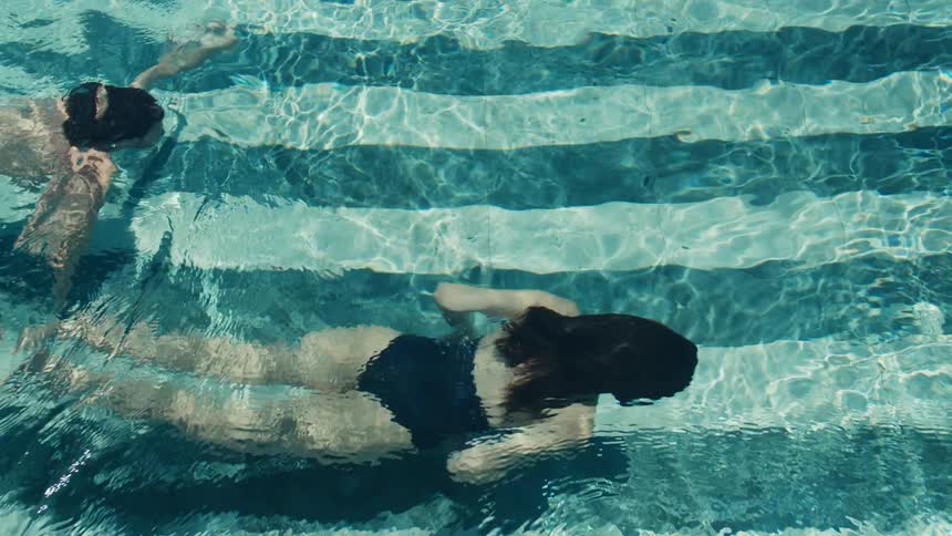 The video shows an overhead shot of two people swimming in a pool with striped tiles the swimmers a man and a woman are doing a leisurely breaststroke sidebyside
