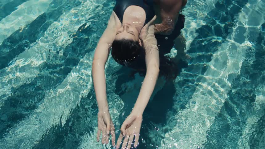 Man holds a woman in a blue swimsuit floating on her back in the pool