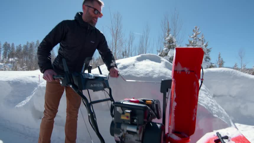 A man uses a snowblower on his driveway