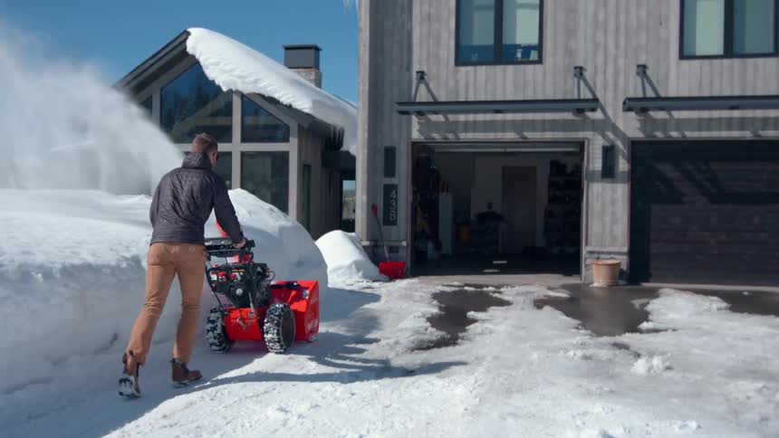 Man clears snow from the house entrance using a snow blower