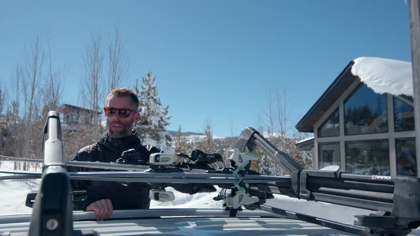 A man loading skis on top of a car preparing to go skiing during winter at midday