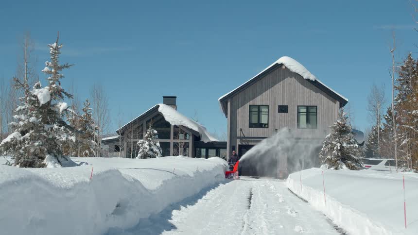 The man is snow blowing his driveway in the rural area