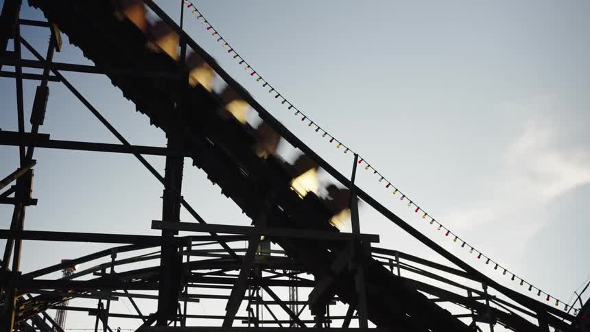 Wooden roller coaster with cars in motion under a clear sky