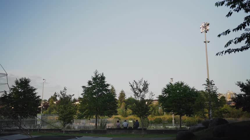 People sit on benches by a suburban sports field at sunset