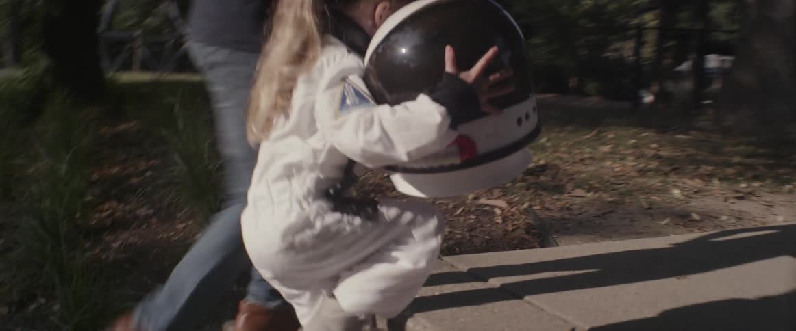 A girl holding a space helmet runs on a sidewalk near a man