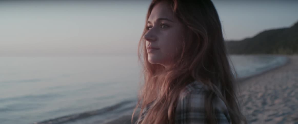 A woman stands on a beach and looks at the ocean