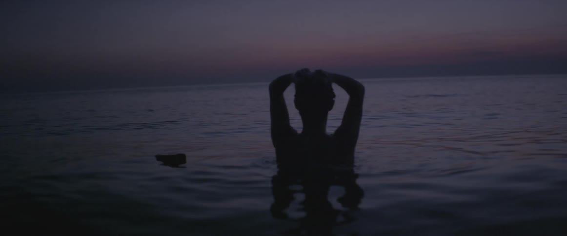A woman shampoos her hair in the ocean