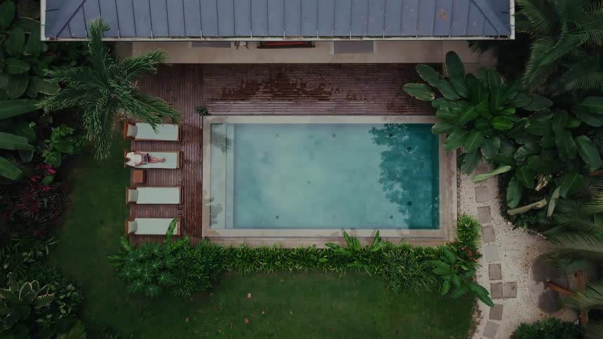 Person relaxes on lounger by pool in tropical yard