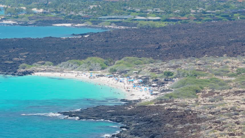 A beach filled with people on an island at midday with waves hitting the shore