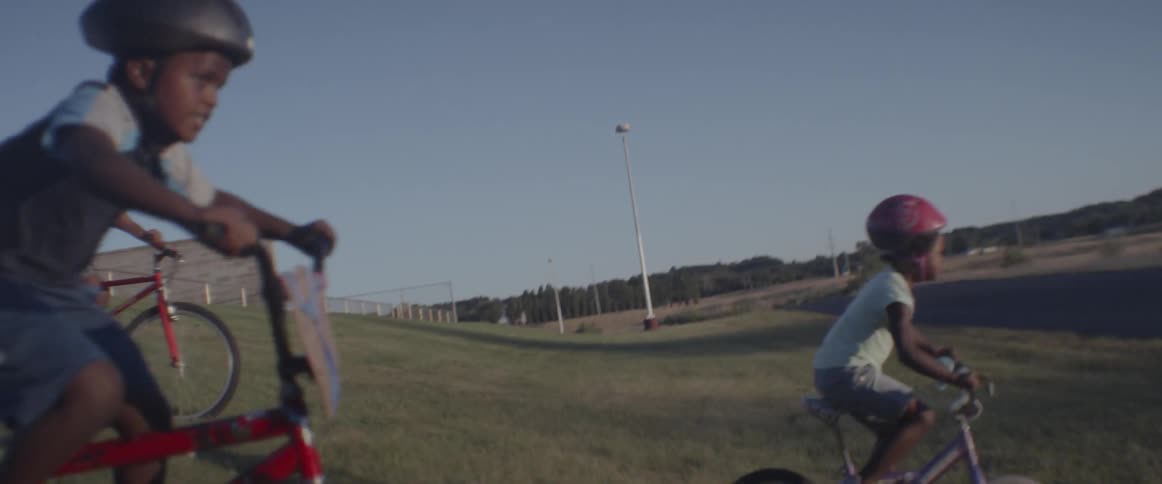 Children ride bikes down a grassy hill