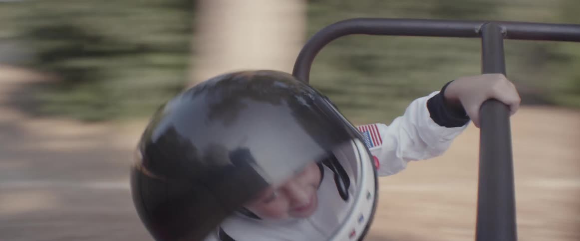 A girl in an astronaut costume spins around on a playground toy