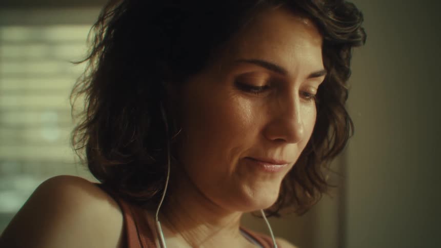 Shorthaired woman wears white earphones while smiling softly