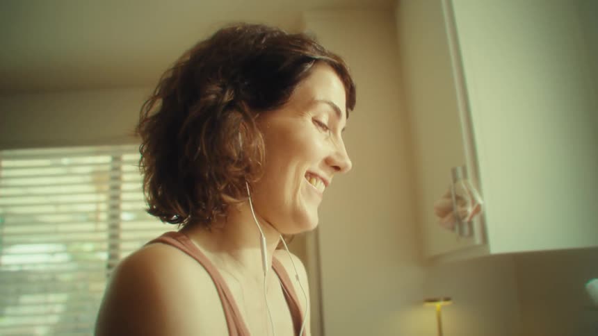 Close up of a young woman listening to music and singing along while doing dishes in the kitchen during daytime