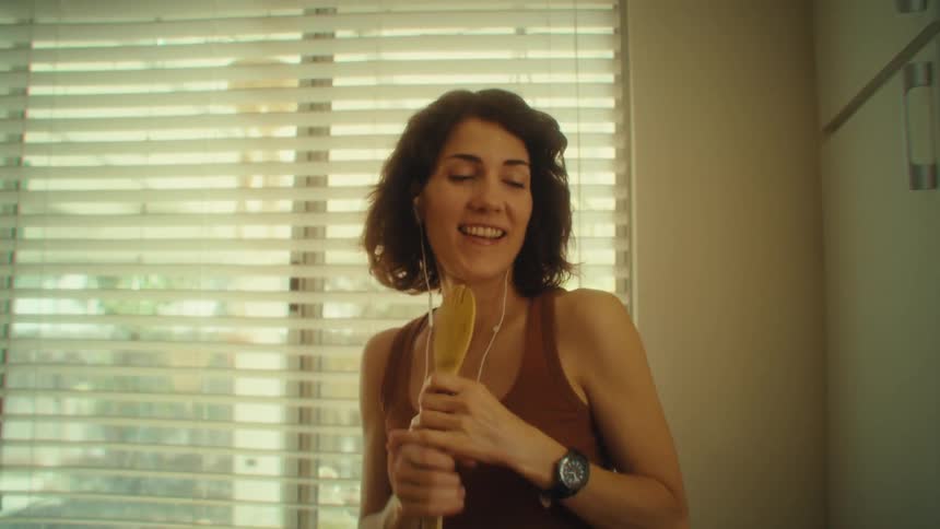 A woman sings passionately into a wooden spoon while grabbing something from the cabinet earbuds in