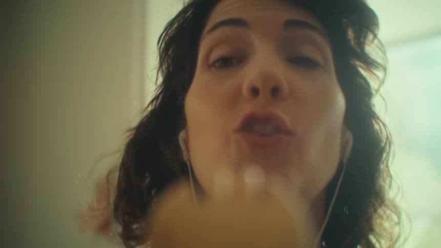 The video shows a closeup of a womans face with her eyes closed as she uses a wooden hairbrush she smiles and looks content suggesting a moment of selfcare or relaxation