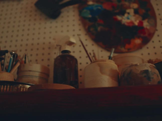Glass jars filled with brushes and pencils sit on a shelf beneath a pegboard in a cozy art studio