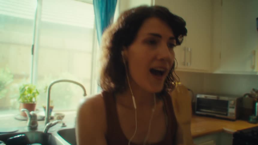 A young woman dancing and having fun in the kitchen at midday singing into a spoon like a microphone