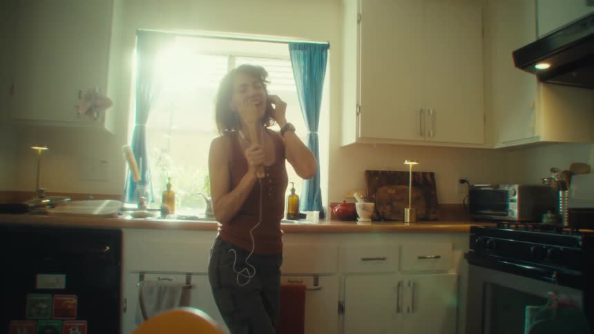 Woman sings and dances in the kitchen holding a wooden utensil as a microphone