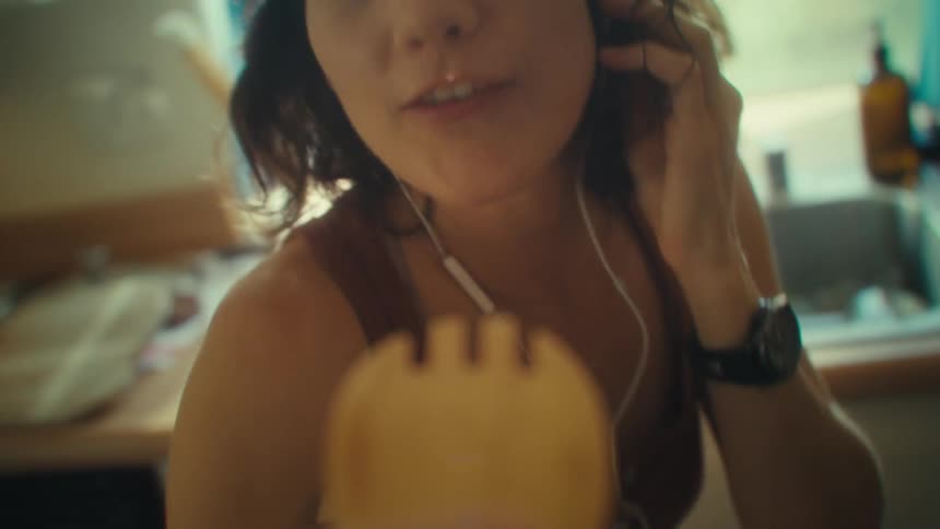 Close up of a young woman singing with a utensil in a kitchen while listening to music with earphones
