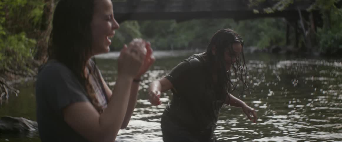 Two women laugh wading in river water