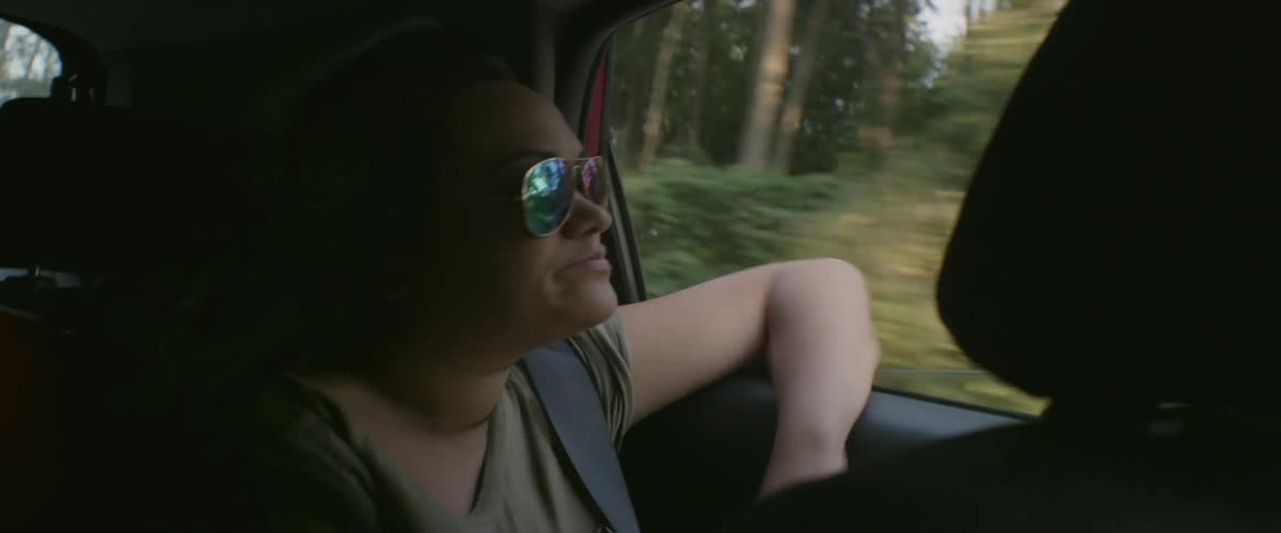 A girl in sunglasses looks out the car window
