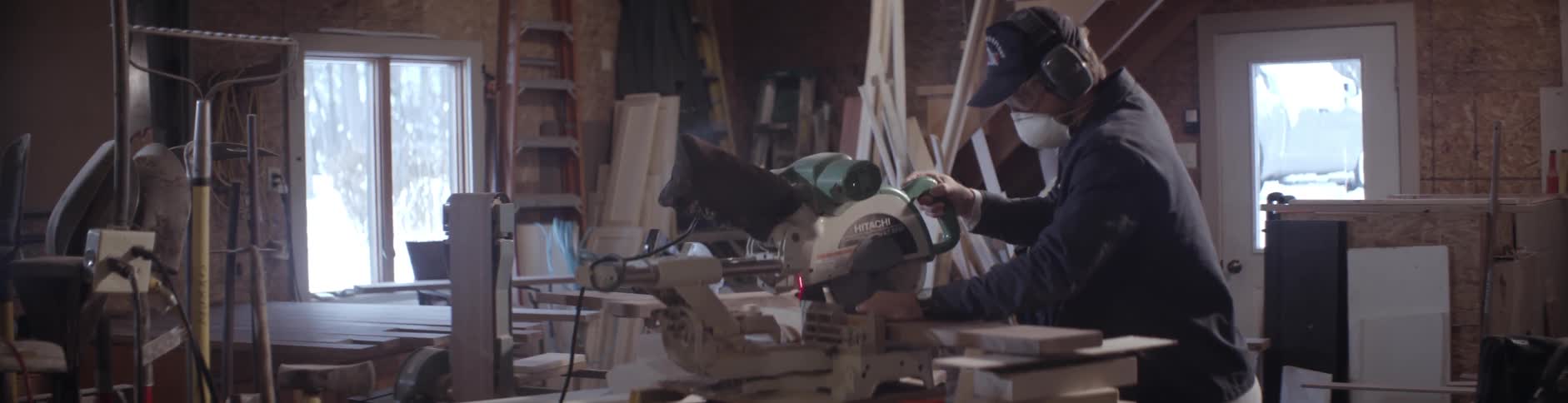 A man wearing a mask cuts a piece of wood