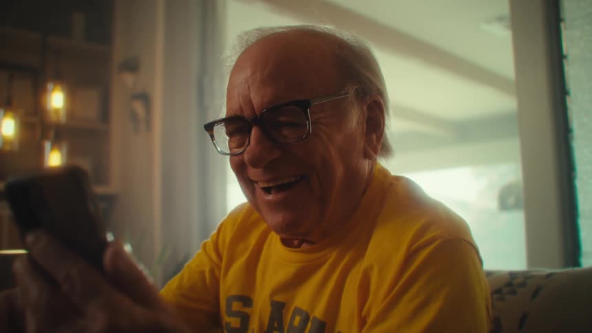 Close up of an elderly man laughing and celebrating while viewing media content on a mobile phone in a living room during daytime