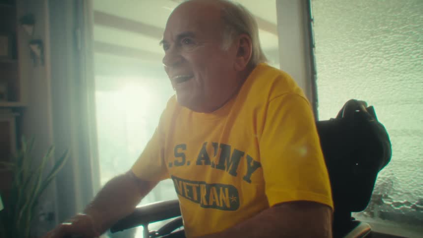 Man in a wheelchair plays video games wearing a yellow army veteran tshirt