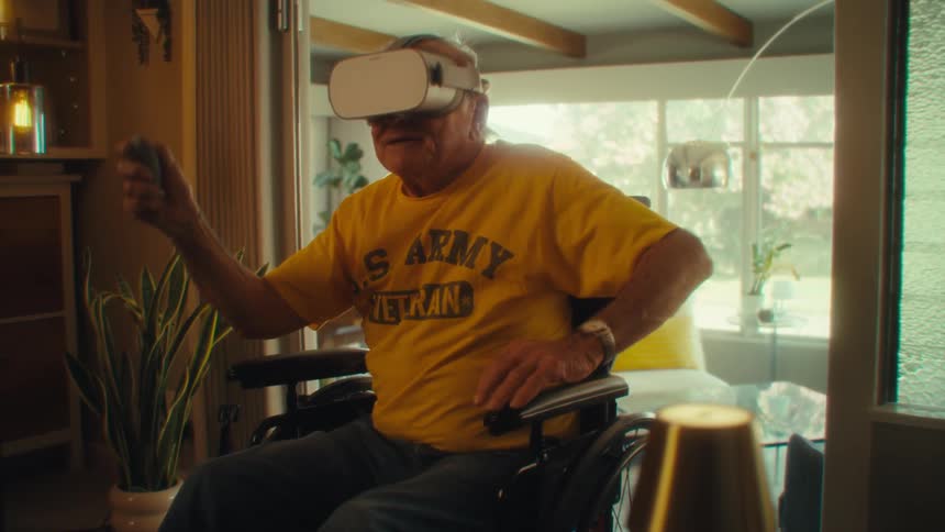 Elderly man in a wheelchair wears virtual reality goggles and holds a controller