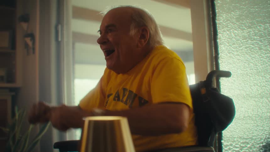 Elderly man in a wheelchair gestures excitedly with a surprised expression