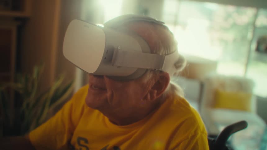 An elderly man wearing a vr headset having fun and excited while sitting in a wheelchair at midday in his living room