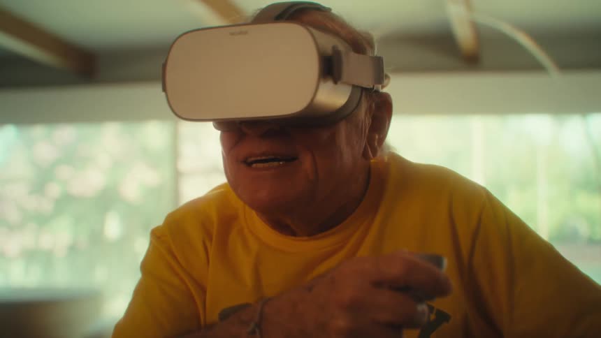 An elderly man sitting in a wheelchair wearing a vr headset and holding a controller having fun