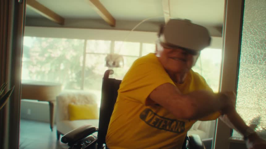 Man in a wheelchair wears virtual reality goggles while pointing with his hand