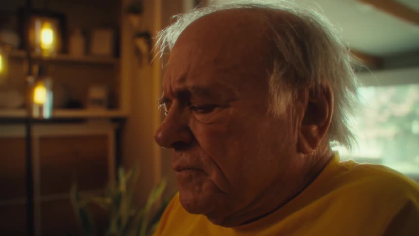 Elderly man in a yellow shirt stares intently with a serious expression