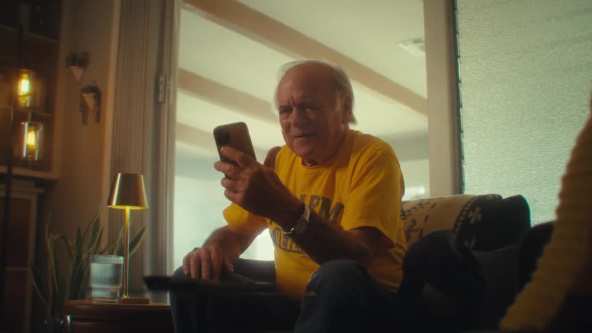 The man is laughing and using his phone at home
