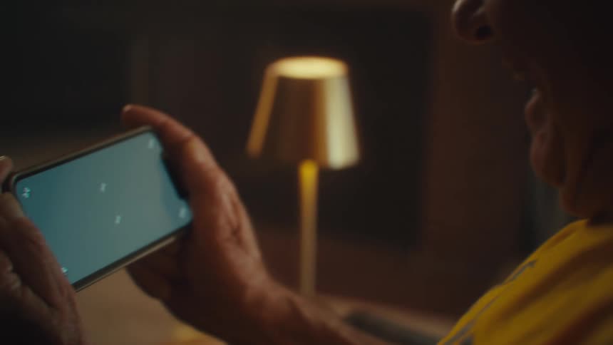 Close up of an elderly man laughing while viewing media content on a phone while sitting in a living room