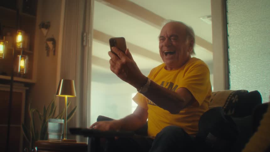 Elderly man laughs excitedly while using a cell phone