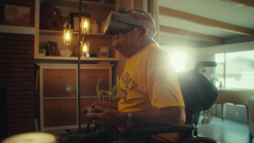Man in a wheelchair wears virtual reality goggles while holding a controller