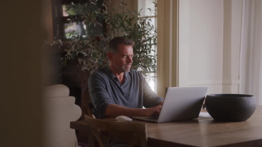 The man looks to his side as he types on the laptop