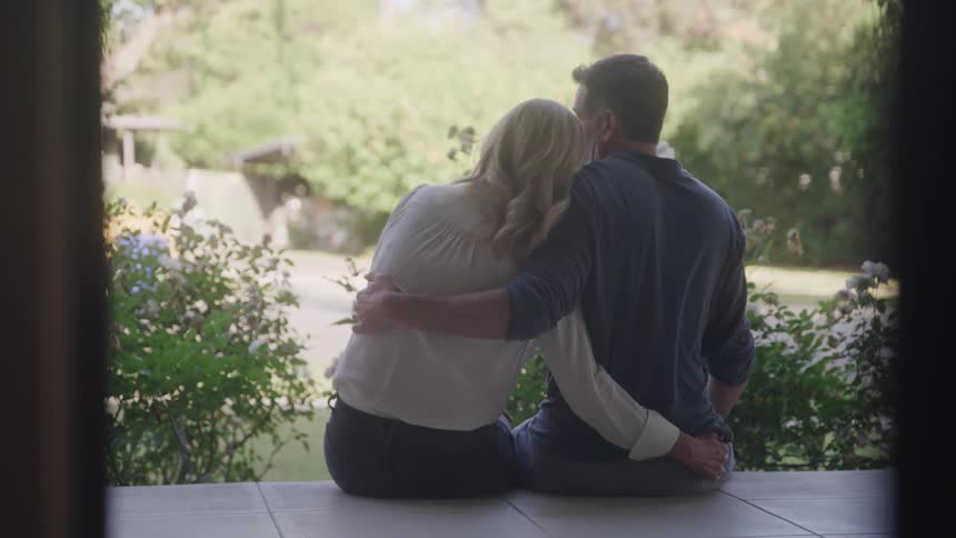 A couple are hugging while sitting on their porch