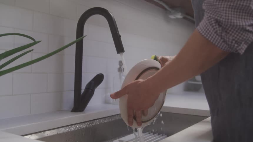 A person rinses a glass dish under running water in a modern white kitchen