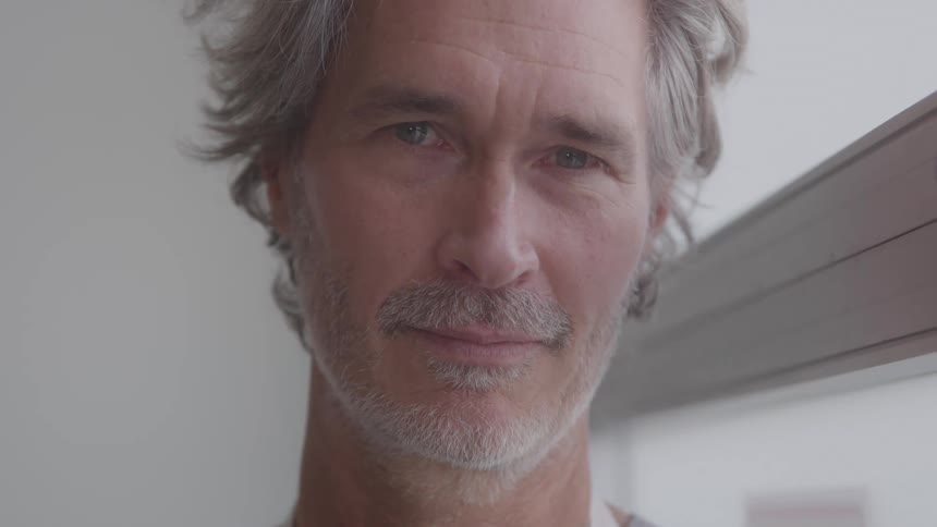 The video shows a man with a beard and graying hair wearing a gray polo shirt he is smiling and looking directly at the camera