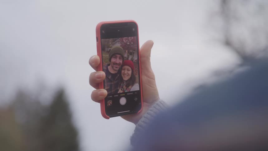 Hand holds up a phone showing a selfie of a smiling couple wearing winter hats