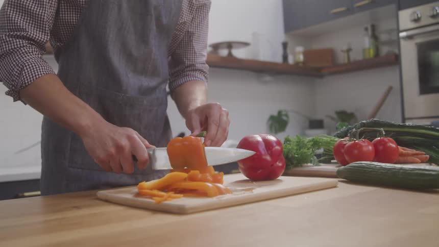 A chef slices a pepper on a chopping board in the kitchen with a knife at midday