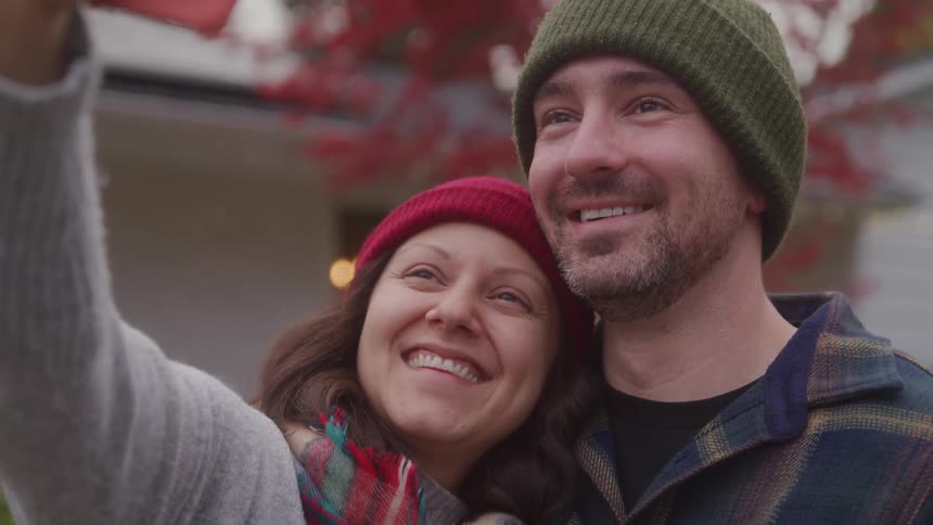 Close up portrait of a man and woman taking a selfie with mobile phone while standing outdoors during daytime