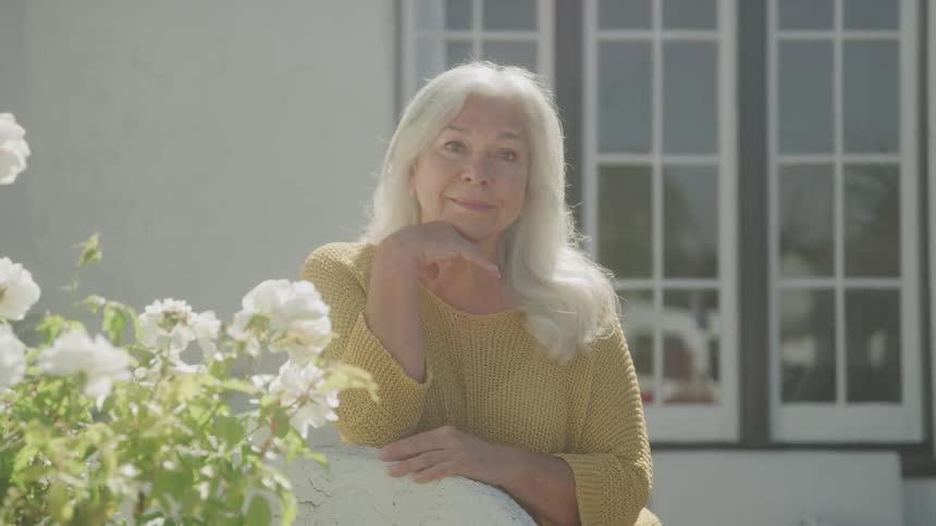 The woman is smiling by the flowers in her yard